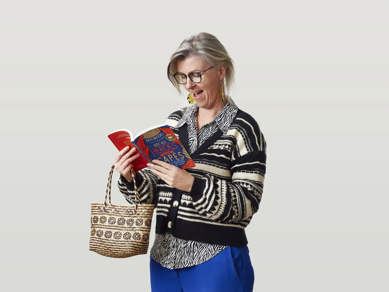 Kowhai reading the book "Not All Heroes Wear Capes" and holding a kete